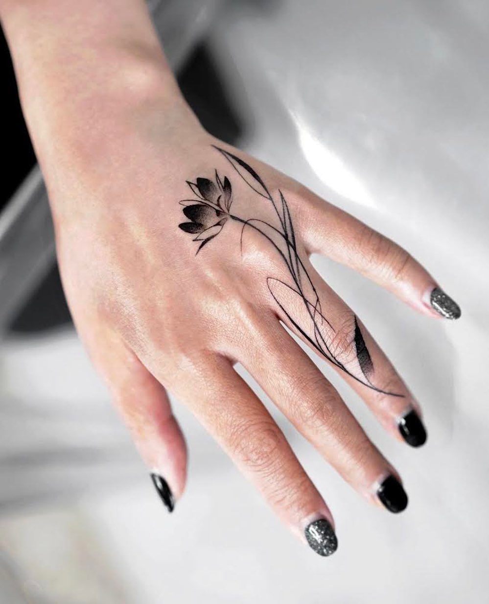 Zwarte Lotus Tattoo op ringvinger en hand