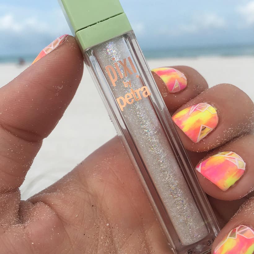 Pixi Liquid Fairy Dust in de hand met nail art op strand