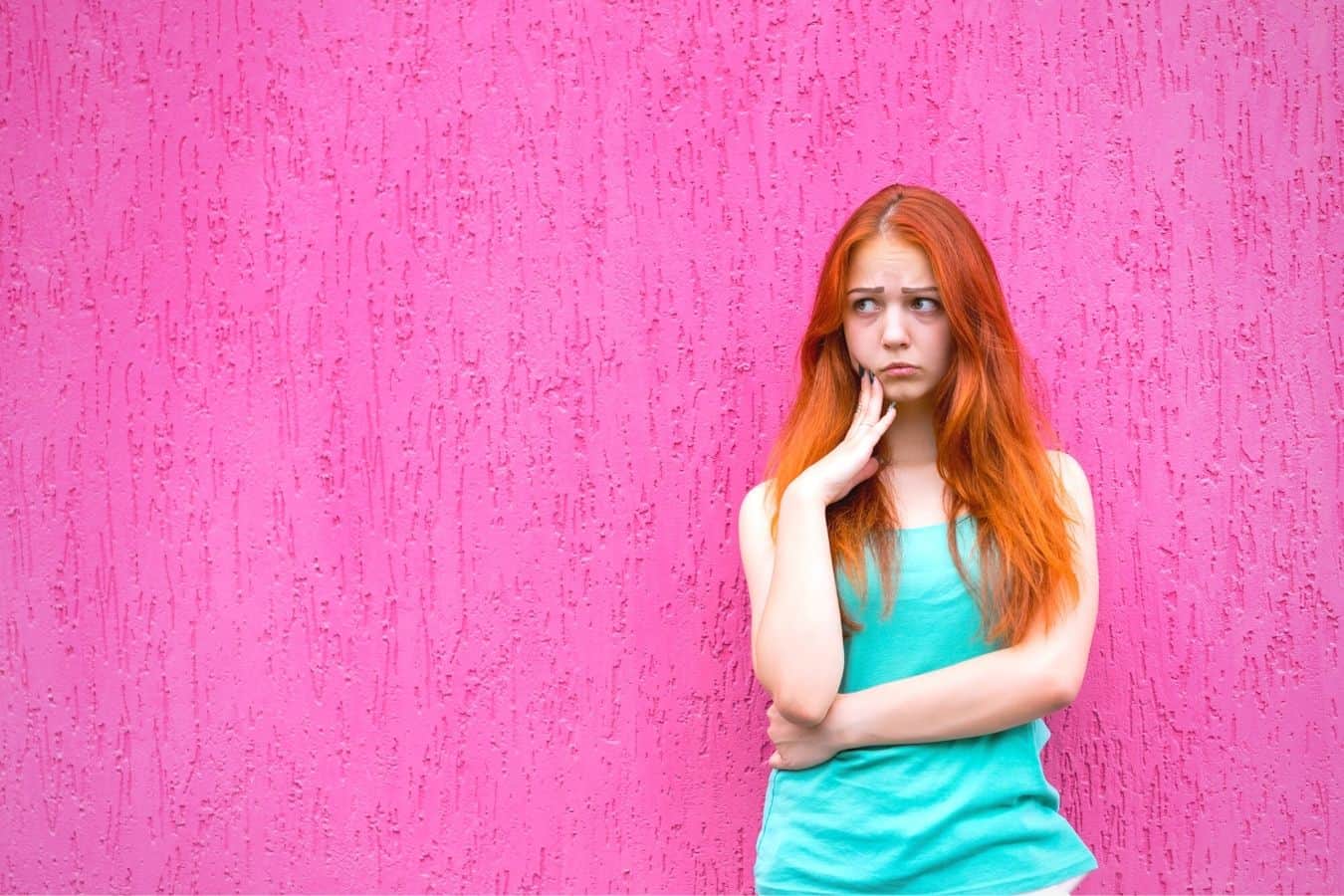 Vrouw met lang rood haar die er verdrietig uitzag, stond voor een roze muur.